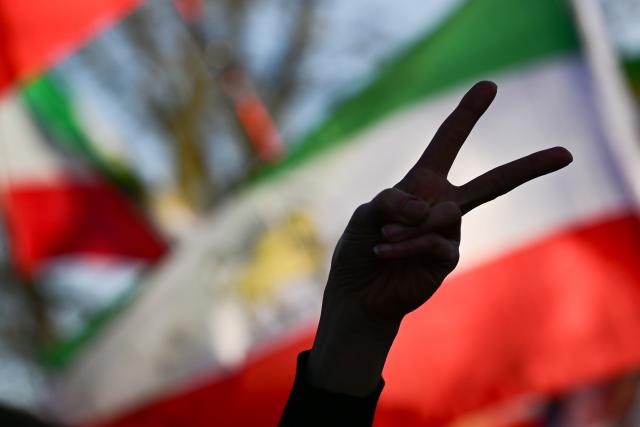 02 March 2026, Berlin: A participant in a demonstration against the Iranian mullah regime displays the victory sign with her hand near the Israeli embassy in front of Iranian flags. Photo: Sebastian Christoph Gollnow/dpa