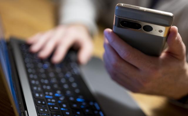 ILLUSTRATION - 27 February 2023, Berlin: A man sits at his laptop and holds a smartphone in his hand. German police have warned travellers about fraud involving fake airline service hotlines after a woman was scammed out of ·2,500 ($2,920) while trying to rebook a flight disrupted by the Iran war. Photo: Monika Skolimowska/dpa