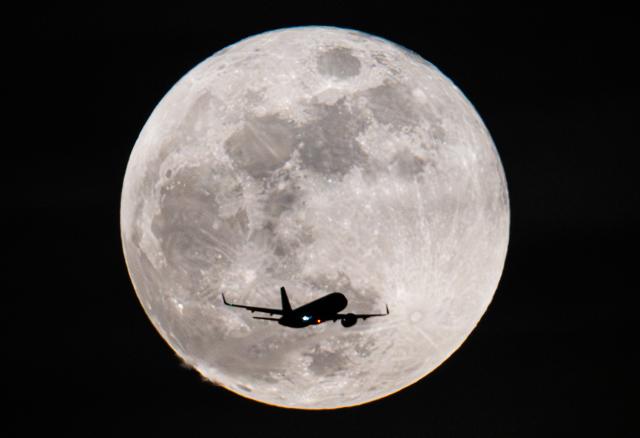 03 March 2026, Hesse, Frankfurt/Main: A passenger plane flies past the full moon on its way to Frankfurt Airport. Photo: Boris Roessler/dpa