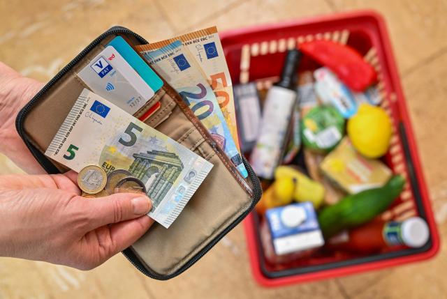 FILED - 21 April 2024, Brandenburg, Sieversdorf: A woman holds money in her hand over of a basket full of groceries. Photo: Patrick Pleul/dpa
