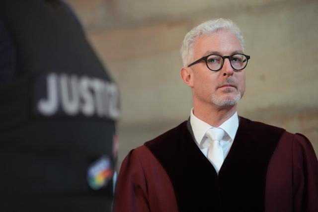 05 March 2026, Hamburg: Stefan Biehl, senior public prosecutor at the Federal Court of Justice (BGH) and representative of the Federal Prosecutor General, stands in the entrance hall of the Hanseatic Higher Regional Court next to a judicial officer, ahead of the trial of the right-wing extremist terrorist group "Letzte Verteidigungswelle" (Last Wave of Defense). Photo: Marcus Brandt/dpa