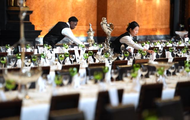 05 March 2026, Hamburg: Linda Nguyen (R), service employee, and Christian Kyei, service employee, place the menu cards on the tables during the final preparations for the Hamburg Senate's traditional Matthiae meal at the town hall. The Hamburg Matthiae banquet is considered to be the oldest banquet still celebrated in the world. The guests of honor at this year's Matthiae-Mahl will be former German Chancellor Merkel and EU Council President Antonio Costa. Photo: Marcus Brandt/dpa