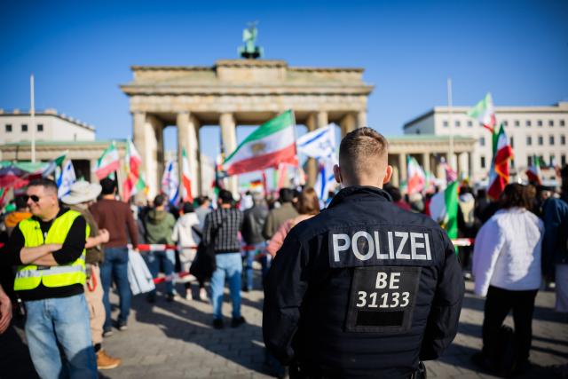 07 March 2026, Berlin: A police officer secures a protest celebrating the killing of Iran's Supreme Leader Ali Khamenei, at the Brandenburg Gate in Berlin. Photo: Christoph Soeder/dpa