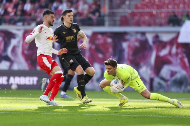 07 March 2026, Saxony, Leipzig: Augsburg goalkeeper Finn Dahmen clears the ball from Leipzigs Romulo Cardoso during the German Bundesliga soccer match between RB Leipzig and FC Augsburg at the Red Bull Arena. Photo: Jan Woitas/dpa - IMPORTANT NOTICE: DFL and DFB regulations prohibit any use of photographs as image sequences and/or quasi-video.