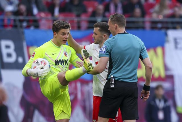 07 March 2026, Saxony, Leipzig: Augsburg goalkeeper Finn Dahmen (L) complains to referee Martin Petersen (R) after an action by Christoph Baumgartner during the German Bundesliga soccer match between RB Leipzig and FC Augsburg at the Red Bull Arena. Photo: Jan Woitas/dpa - IMPORTANT NOTICE: DFL and DFB regulations prohibit any use of photographs as image sequences and/or quasi-video.