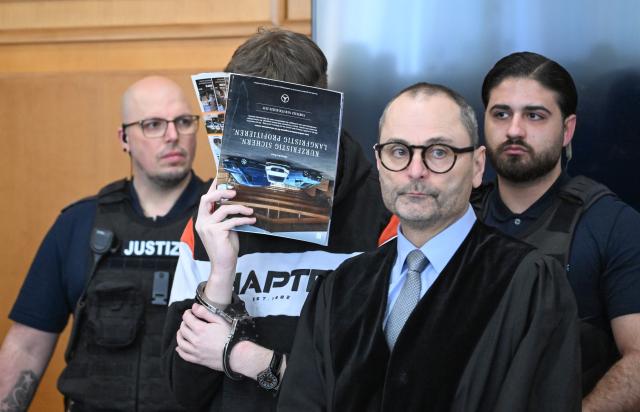 11 March 2026, Baden-Wuerttemberg, Heilbronn: A defendant (2nd L) stands in front of his lawyer Andreas Kugel (2nd R) in the courtroom with a newspaper covering his face before the start of his trial. The defendant, who was 18 at the time of the crime, is alleged to have deliberately driven his car into a 12-year-old boy who was riding his bicycle ahead of him in the parking lot of a supermarket in Niedernhall in September 2025. Photo: Bernd Weißbrod/dpa