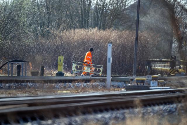12 March 2026, Bavaria, Bayreuth: A man wearing a high-visibility vest carries a barrier onto a track, following a collision between two regional trains. Photo: Pia Bayer/dpa
