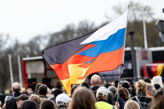 14 March 2026, Berlin: Participants at the "Transparency, Rule of Law, and Protection of Minors" demonstration carry a flag divided into the colors of Germany and Russia while calling for "an investigation into possible German connections to the international Epstein scandal." Photo: Fabian Sommer/dpa