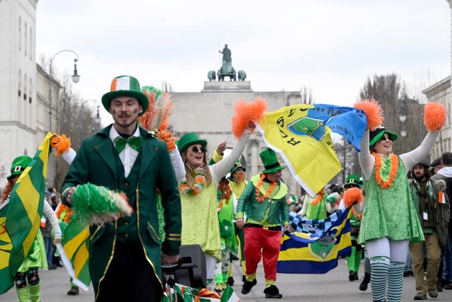 15 March 2026, Bavaria, Munich: Participants in the St. Patrick's Day parade pass the Siegestor on their way from Muenchner Freiheit to Odeonsplatz. The parade in Munich in honor of the Irish national saint is celebrating its 30th anniversary this year. Photo: Felix Hörhager/dpa
