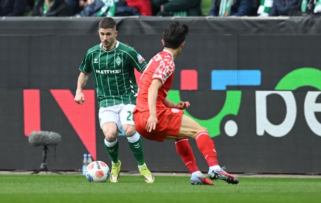 15 March 2026, Bremen: Werder Bremen's Romano Schmid (L) and Mainz's Jae-sung Lee battle for the ball during the German Bundesliga soccer match between Werder Bremen and FSV Mainz 05 at Weserstadion. Photo: Carmen Jaspersen/dpa - WICHTIGER HINWEIS: Gemäß den Vorgaben der DFL Deutsche Fußball Liga bzw. des DFB Deutscher Fußball-Bund ist es untersagt, in dem Stadion und/oder vom Spiel angefertigte Fotoaufnahmen in Form von Sequenzbildern und/oder videoähnlichen Fotostrecken zu verwerten bzw. verwerten zu lassen.
