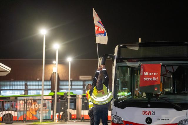 17 March 2026, North Rhine-Westphalia, Dormtund: Strikers attach a Verdi union flag to a bus during a warning strike. Photo: Max Lametz/dpa