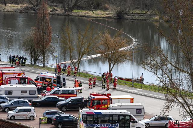 17 March 2026, Saxony-Anhalt, Wettin: Fire department vehicles are stationed on the banks of the Saale River as an oil boom is deployed on the water after an oil slick is discovered. Fire departments from Saalekreis and Salzatal prevent it from spreading further. Ferry services are temporarily suspended. Photo: Heiko Rebsch/dpa