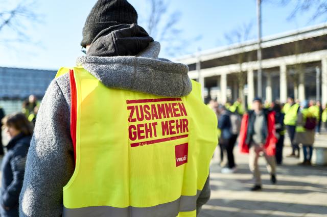18 March 2026, Brandenburg, Schoenefeld: Striking airport employees and Verdi union members stand in front of the terminal during a warning strike at Berlin Brandenburg Airport (BER), halting all operations. No passenger flights have taken off or landed at BER since this morning, with all departures and arrivals cancelled for the entire day, the Berlin-Brandenburg Airport Company (FBB) had announced. Photo: Michael Ukas/dpa
