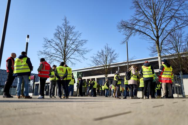18 March 2026, Brandenburg, Schoenefeld: Striking airport employees and Verdi union members stand in front of the terminal during a warning strike at Berlin Brandenburg Airport (BER), halting all operations. No passenger flights have taken off or landed at BER since this morning, with all departures and arrivals cancelled for the entire day, the Berlin-Brandenburg Airport Company (FBB) had announced. Photo: Michael Ukas/dpa