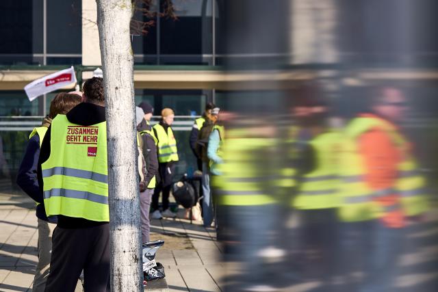 18 March 2026, Brandenburg, Schoenefeld: Striking airport employees and Verdi union members stand in front of the terminal during a warning strike at Berlin Brandenburg Airport (BER), halting all operations. No passenger flights have taken off or landed at BER since this morning, with all departures and arrivals cancelled for the entire day, the Berlin-Brandenburg Airport Company (FBB) had announced. Photo: Michael Ukas/dpa