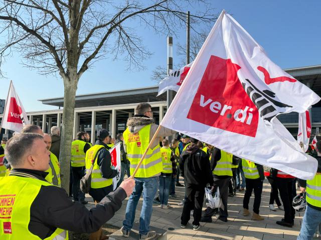18 March 2026, Brandenburg, Schoenefeld: Striking airport employees and Verdi union members stand in front of the terminal during a warning strike at Berlin Brandenburg Airport (BER), halting all operations. No passenger flights have taken off or landed at BER since this morning, with all departures and arrivals cancelled for the entire day, the Berlin-Brandenburg Airport Company (FBB) had announced. Photo: Marvin Zubrod/dpa