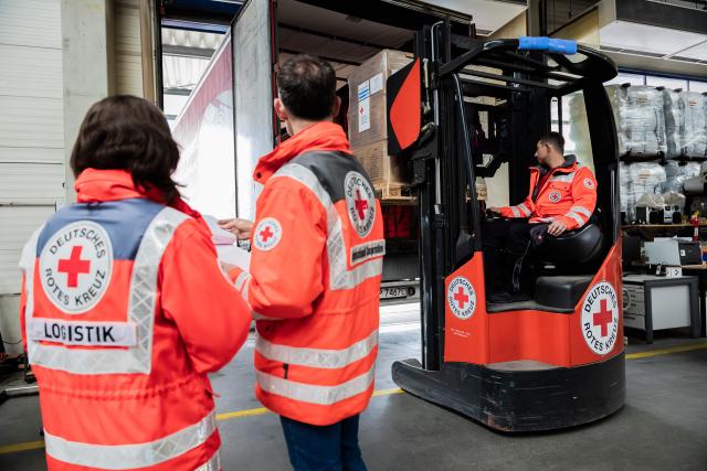 20 March 2026, Brandenburg, Schönefeld: Relief supplies for Lebanon are loaded with a forklift truck at the German Red Cross logistics center at Berlin-Schoenefeld Airport while employees stand next to it for a TV camera shoot. Around 30 tons of relief supplies are loaded, transported first by truck to Maastricht and from there via an EU air bridge to Beirut. Photo: Christoph Soeder/dpa