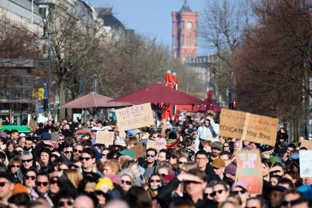 22 March 2026, Berlin: A sign reading "Down with the Patriarchy" (C) is seen during a demonstration against sexualized digital violence in front of the Brandenburg Gate. Photo: Carsten Koall/dpa