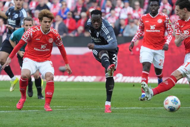 22 March 2026, Rhineland-Palatinate, Mainz: Eintracht Frankfurt's Arnaud Kalimuendo (C) takes a shot past Mainz's Kaishu Sano (L) and Dominik Kohr (R) during the German Bundesliga soccer match between FSV Mainz 05 and Eintracht Frankfurt at the Mewa Arena. Photo: Marc Schüler/dpa - IMPORTANT NOTICE: DFL and DFB regulations prohibit any use of photographs as image sequences and/or quasi-video.