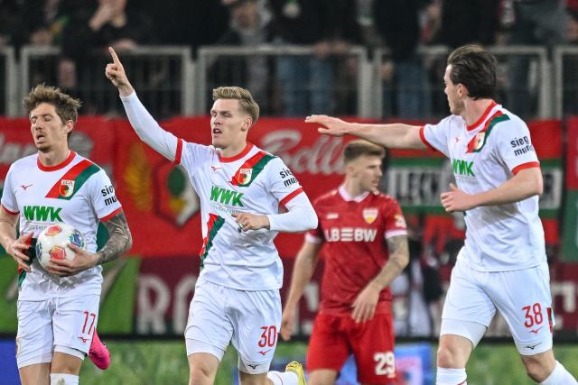 22 March 2026, Bavaria, Augsburg: Augsburg's Anton Kade (C) celebrates his side's second goal of the game with his teammates Kristijan Jakic (L) and Michael Gregoritsch during the German Bundesliga match between FC Augsburg and VfB Stuttgart at the Millerntor Stadium. Photo: Harry Langer/dpa - WICHTIGER HINWEIS: Gemäß den Vorgaben der DFL Deutsche Fußball Liga bzw. des DFB Deutscher Fußball-Bund ist es untersagt, in dem Stadion und/oder vom Spiel angefertigte Fotoaufnahmen in Form von Sequenzbildern und/oder videoähnlichen Fotostrecken zu verwerten bzw. verwerten zu lassen.