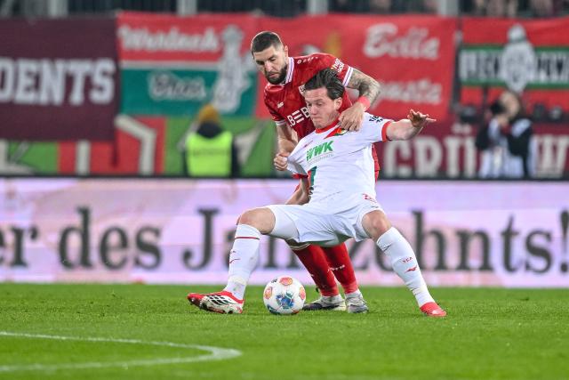 22 March 2026, Bavaria, Augsburg: Stuttgart's Jeff Chabot (L) and Augsburg's Michael Gregoritsch battle for the ball during the German Bundesliga match between FC Augsburg and VfB Stuttgart at the Millerntor Stadium. Photo: Harry Langer/dpa - WICHTIGER HINWEIS: Gemäß den Vorgaben der DFL Deutsche Fußball Liga bzw. des DFB Deutscher Fußball-Bund ist es untersagt, in dem Stadion und/oder vom Spiel angefertigte Fotoaufnahmen in Form von Sequenzbildern und/oder videoähnlichen Fotostrecken zu verwerten bzw. verwerten zu lassen.