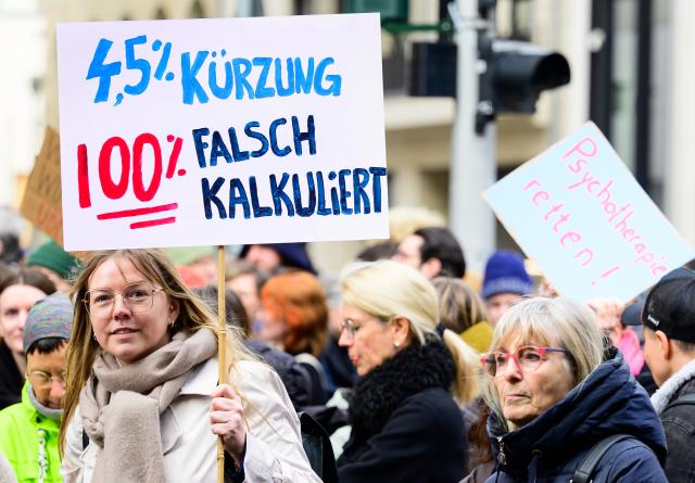 26 March 2026, Berlin: Participants in a rally organized by the Psychotherapy Action Alliance demonstrate outside the Germany's Ministry of Health against cuts to the fees of outpatient psychotherapists, holding signs reading, among other things, '4.5 percent cut: 100 percent miscalculated.' Photo: Soeren Stache/dpa