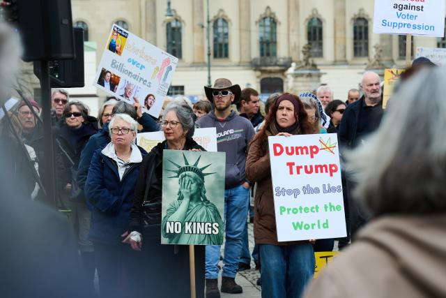 28 March 2026, Berlin: A protester holds a sign reading 'Dump Trump - Stop the Lies - Protect the World' on Bebelplatz during a demonstration against the Trump administration. Protests against President Donald Trump's policies are taking place in Germany as well as in many US cities and other locations worldwide. Photo: Annette Riedl/dpa