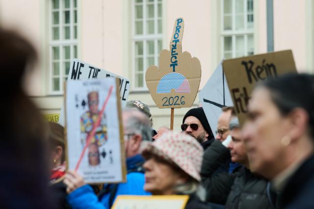 28 March 2026, Berlin: A protester holds a poster reading 'Protect 2026,' depicting a German government with an AfD majority, during a demonstration against the Trump administration. Protests against President Donald Trump's policies are taking place in Germany as well as in many US cities and other locations worldwide. Photo: Annette Riedl/dpa