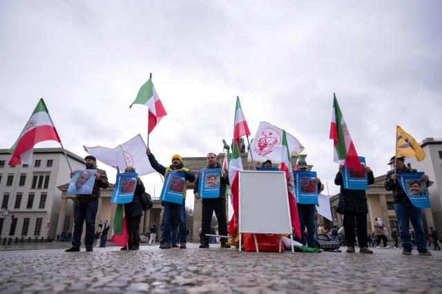 31 March 2026, Berlin: Participants in a rally titled 'Stop the Massacre of Political Prisoners in Iran' hold flags and signs in front of the Brandenburg Gate, protesting the execution of political prisoners in Iran. Photo: Christophe Gateau/dpa