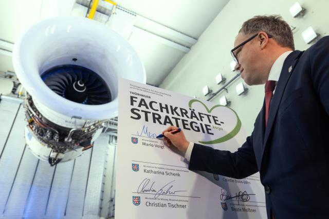 01 April 2026, th, Arnstadt: Mario Voigt, Minister-President of Thuringia (4th L), signs a skilled workforce strategy in front of a Trent 900 engine in the test tower of N3 Engine Overhaul Services GmbH during a meeting of the Pact for Growth and Jobs. Photo: Michael Reichel/dpa