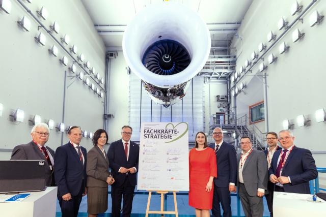 01 April 2026, th, Arnstadt: Representatives from the state government, the business community, and labour unions pose with Mario Voigt, Minister-President of Thuringia (4th L), in front of a Trent 900 engine in the test tower of N3 Engine Overhaul Services GmbH following the signing of a skilled workforce strategy. The event takes place as part of a meeting of the Pact for Growth and Jobs. Photo: Michael Reichel/dpa