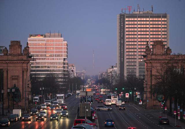 02 April 2026, Berlin: The rising sun casts an orange glow on the windows of the high-rises along Strasse des 17. Juni behind Charlottenburger Tor. Photo: Soeren Stache/dpa