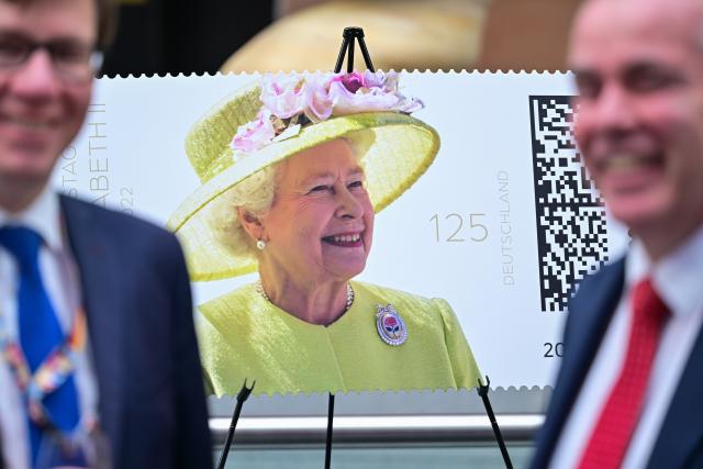 02 April 2026, Berlin: An oversized replica of the Queen stamp stands behind two men during the unveiling of a special stamp commemorating "Her Majesty Queen Elizabeth II's 100th Birthday" at the British Embassy. Photo: Sebastian Christoph Gollnow/dpa