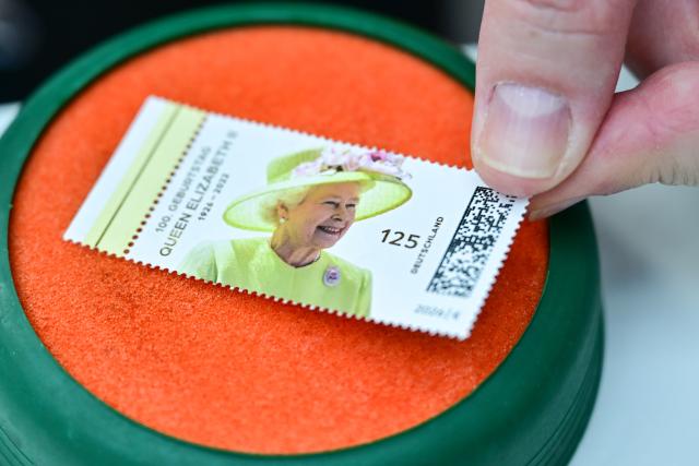 02 April 2026, Berlin: A woman is licking a Queen stamp during the unveiling of a special stamp commemorating "Her Majesty Queen Elizabeth II's 100th Birthday" at the British Embassy. Photo: Sebastian Christoph Gollnow/dpa