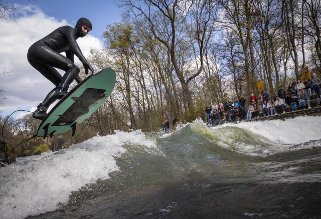 03 April 2026, Bavaria, Munich: A man attempts to jump onto the makeshift Eisbach wave in the English Garden with a big leap. Photo: Peter Kneffel/dpa
