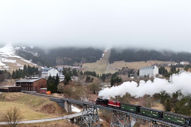 04 April 2026, Saxony, Oberwiesenthal: The Fichtelbergbahn passes the Huettenbach viaduct in front of Oberwiesenthal station, with the fog-covered Fichtelberg in the background. Special trips on the narrow-gauge railroad are planned for the Easter weekend. Photo: Sebastian Willnow/dpa