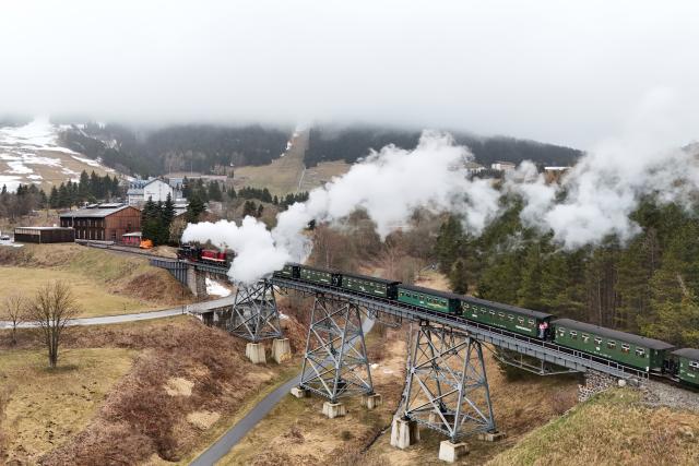 04 April 2026, Saxony, Oberwiesenthal: The Fichtelbergbahn passes the Huettenbach viaduct in front of Oberwiesenthal station, with the fog-covered Fichtelberg in the background. Special trips on the narrow-gauge railroad are planned for the Easter weekend. Photo: Sebastian Willnow/dpa
