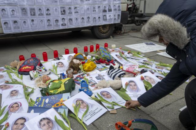 04 April 2026, Bavaria, Munich: A woman places a flower next to the portraits of girls who were killed in the bombing of a girls' school in Iran at the Easter March rally on Marienplatz. Photo: Stefan Puchner/dpa