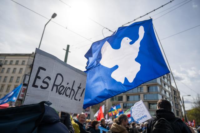 04 April 2026, Berlin: A participant holds a sign reading "Enough is enough!", which can be seen next to a flag featuring a dove of peace during the "Demonstration for Peace" Easter March. Photo: Christophe Gateau/dpa