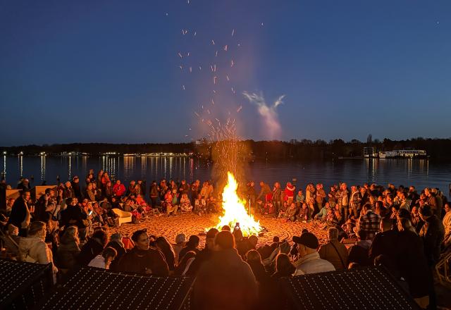 04 April 2026, Berlin: Visitors sit around the Easter bonfire at the Wendenschloss lido. Photo: Britta Pedersen/dpa