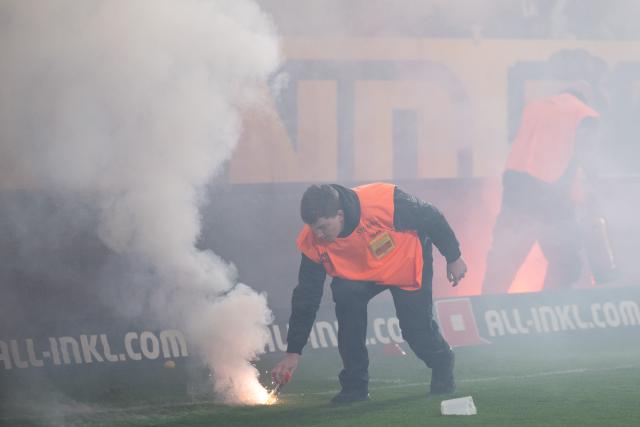 04 April 2026, Saxony, Dresden: A stadium employee removes burning pyrotechnics from the pitch during a stoppage at the German 2nd Bundesliga soccer match between Dynamo Dresden and Hertha BSC, at the Rudolf-Harbig-Stadium. Photo: Sebastian Kahnert/dpa - IMPORTANT NOTICE: DFL and DFB regulations prohibit any use of photographs as image sequences and/or quasi-video.
