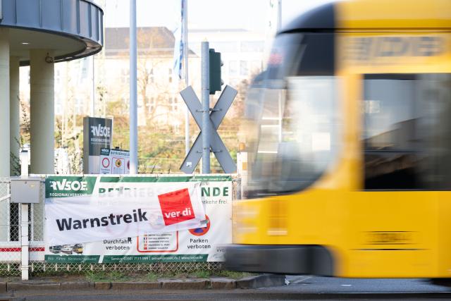 09 April 2026, Saxony, Dresden: A streetcar operated by Dresdner Verkehrsbetriebe (DVB) passes a banner reading "Warning strike" during a warning strike by Regional Transport Saechsische Schweiz-Osterzgebirge (RVSOE). The background to this is the deadlocked wage negotiations with the local transport employers' association (AVN Group), in which, according to Verdi, no agreement was reached in the fifth round of negotiations. Photo: Sebastian Kahnert/dpa