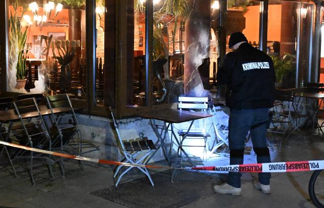 10 April 2026, Bavaria, Munich: A detective is standing in front of an Israeli restaurant, holding a flashlight, after the restaurant's window has been smashed. Photo: Felix Hörhager/dpa