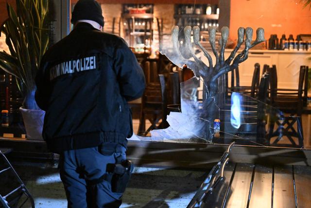 10 April 2026, Bavaria, Munich: A detective is standing in front of an Israeli restaurant, holding a flashlight, after the restaurant's window has been smashed. Photo: Felix Hörhager/dpa