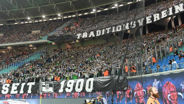 FILED - 20 September 2016, Saxony, Leipzig: Borussia Moenchengladbach fans unfurl a banner reading 'Traditional club, since 1900' and cheer on their team after 20 minutes of silence in the stands during the German Bundesliga soccer match against RB Leipzig at the Red Bull Arena. Fans had been asked to refrain from purchasing food and drinks in the stadium in order not to financially support the Red Bull-backed club. Photo: Hendrik Schmidt/dpa