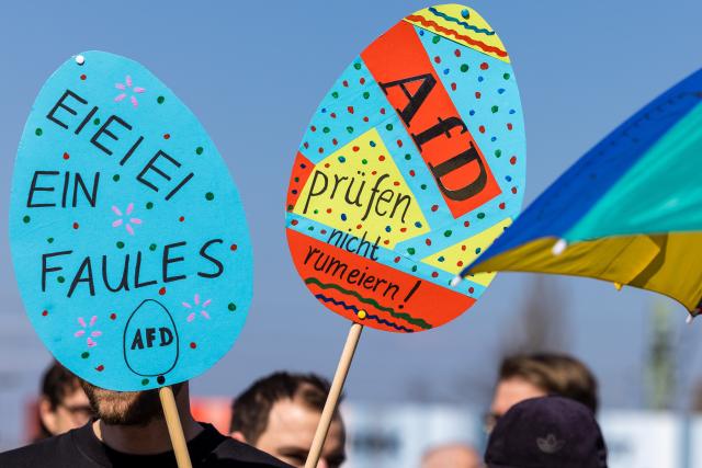 11 April 2026, Brandenburg, Cottbus: A man holds a sign reading 'Don't dither on investigating the AfD' during a demonstration at the main train station. The protest calls for an investigation into and a ban on the AfD, whose parliamentary group in the Bundestag gathered in the city for a three-day closed-door meeting. Photo: Frank Hammerschmidt/dpa