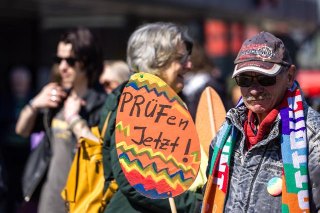 11 April 2026, Brandenburg, Cottbus: 'Check Now' is written on a cardboard egg carried by a man during a demonstration at the main train station. The protest calls for an investigation into and a ban on the AfD, whose parliamentary group met in the city for a three-day closed-door meeting. Photo: Frank Hammerschmidt/dpa