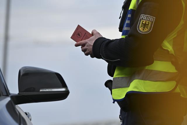 FILED - 17 December 2025, Baden-Württemberg, Kehl: A German police officer checks a car at the border between France and Germany during a photo session with the German Press Agency, holding a French driver's license in his hands. Romanian police fined a driver for speeding who explained she had to hurry or her cake would burn. Photo: Katharina Kausche/dpa