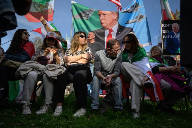 11 April 2026, Hesse, Frankfurt/Main: Participants stand in front of a banner featuring Donald Trump and fighter jets during a pro-U.S. and pro-Shah rally in front of the US Consulate General in Frankfurt am Main. Photo: Hannes P. Albert/dpa