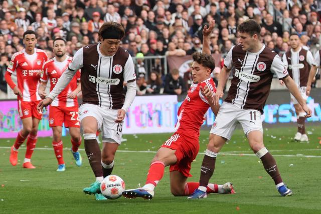 11 April 2026, Hamburg: Bayern Munich's Tom Bischof in action against St. Pauli's Tomoya Ando and Arkadiusz Pyrka in action during the German Bundesliga soccer match between FC St. Pauli and Bayern Munich at Millerntor Stadium. Photo: Christian Charisius/dpa - IMPORTANT NOTICE: DFL and DFB regulations prohibit any use of photographs as image sequences and/or quasi-video.